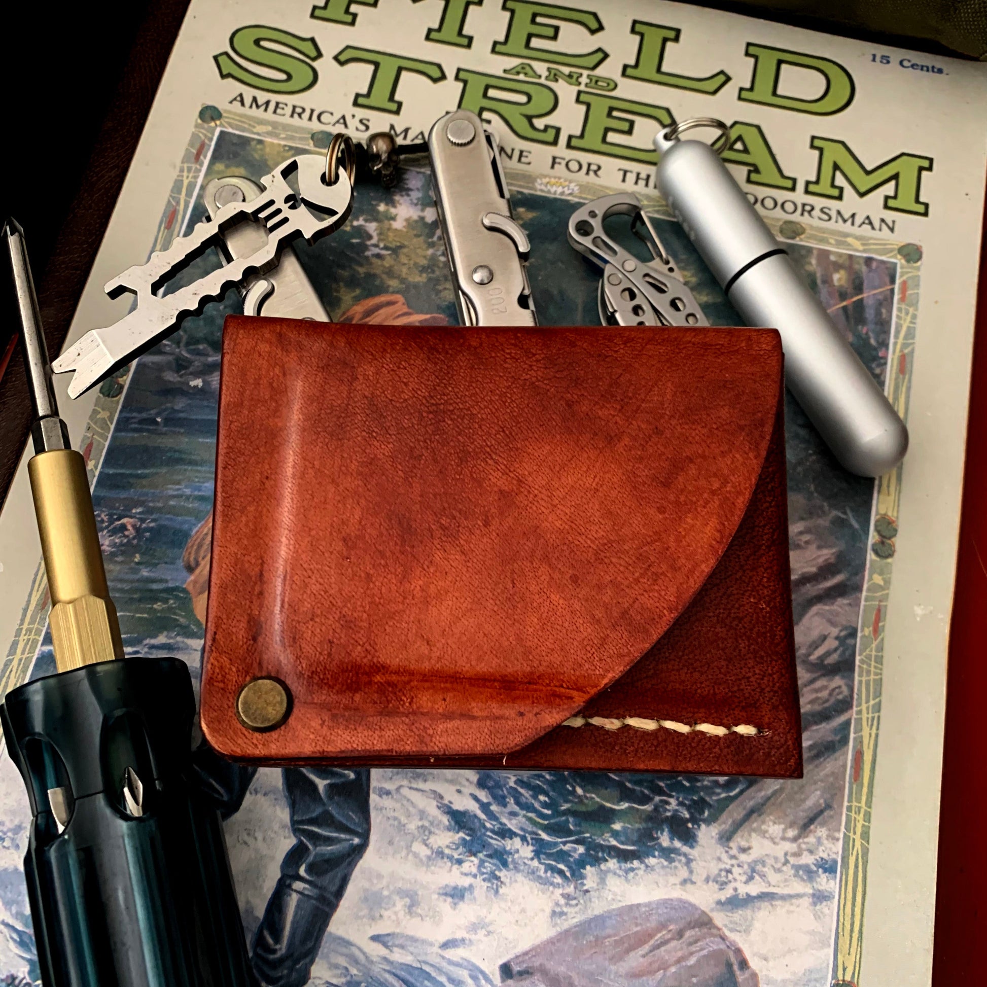 Brown leather wallet on a 'Field & Stream' magazine with various items including keys and a pen.