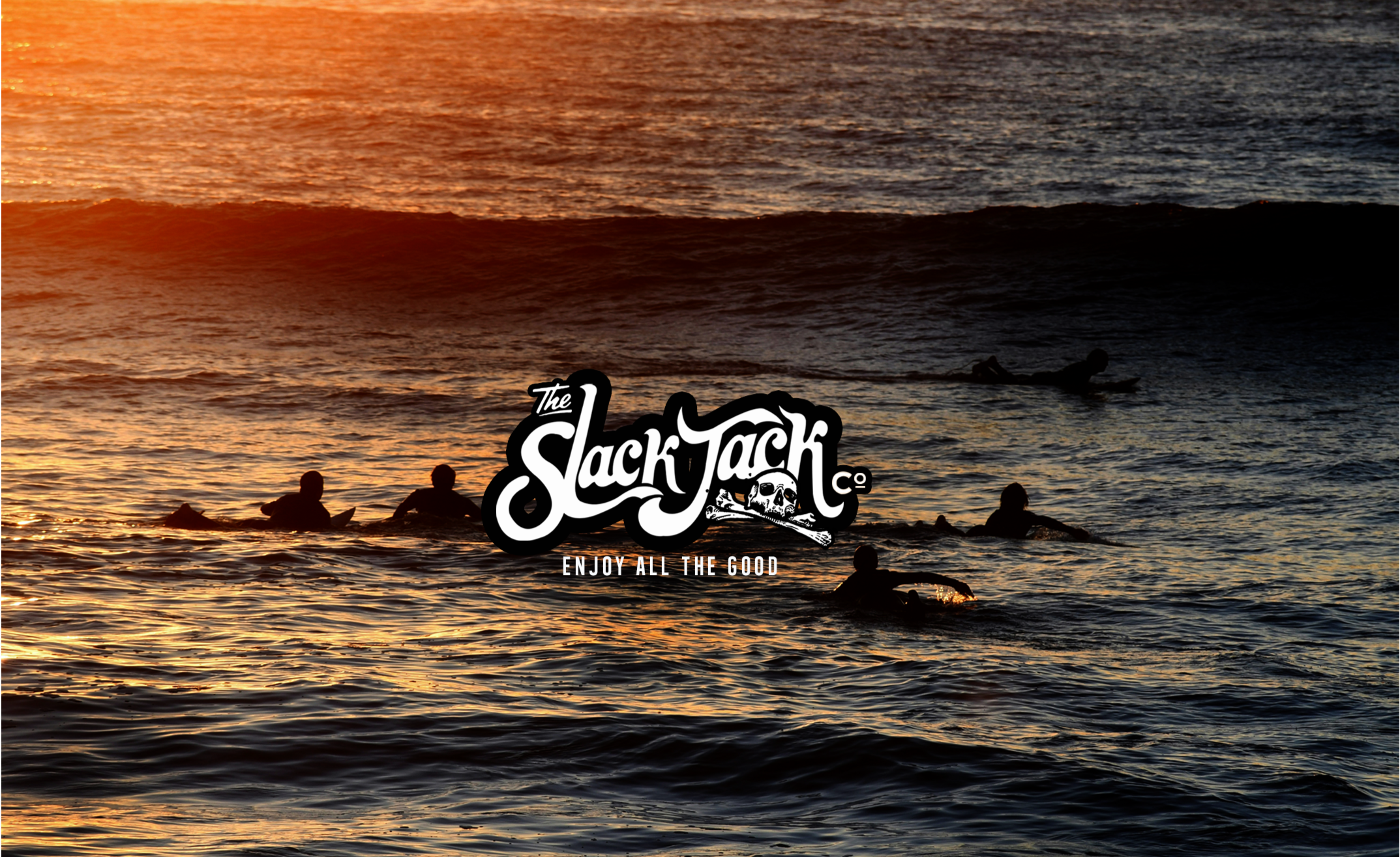 Surfers in the ocean at sunset with 'The Slack Jack Co.' logo.